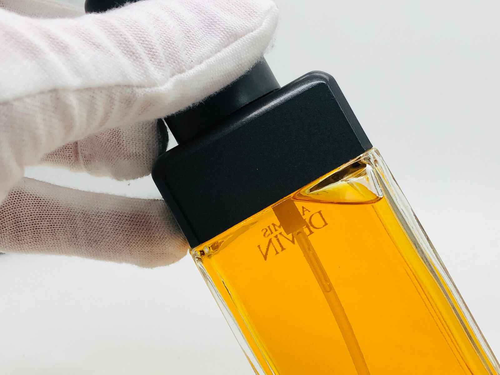 Flacone di profumo Aramis Devin Country con tappo nero e liquido dorato, in mano con guanto bianco