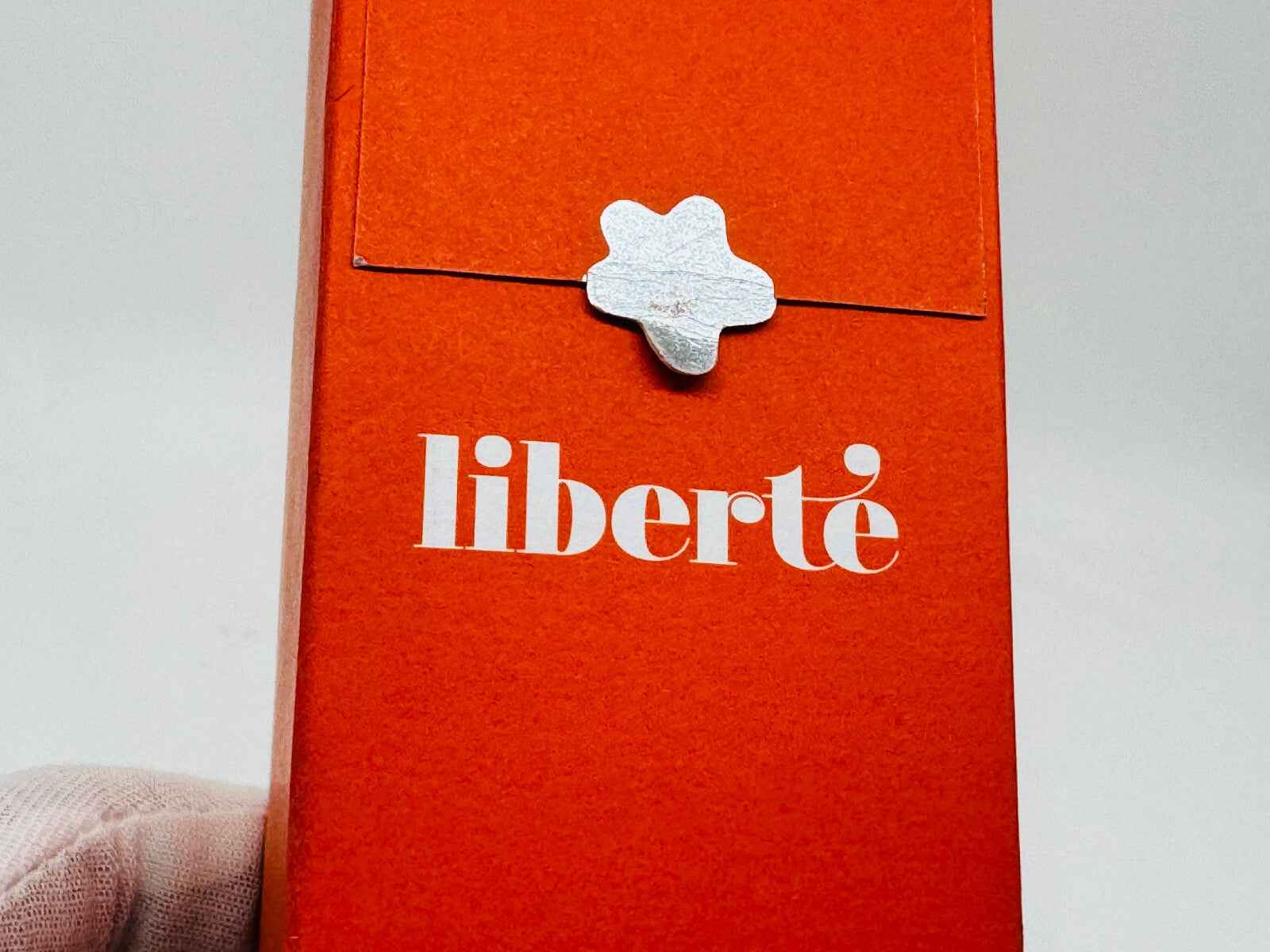 Scatola arancione del profumo Cacharel Liberte Vintage con chiusura decorativa stilizzata