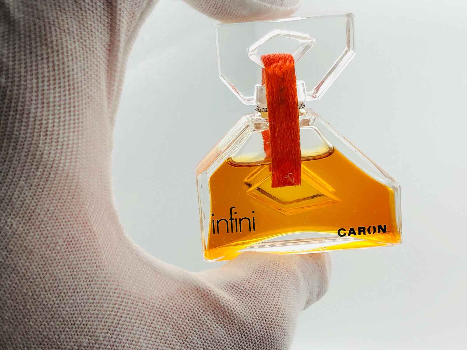 Profumo Infini Caron in bottiglia trasparente con etichetta arancione e liquido dorato