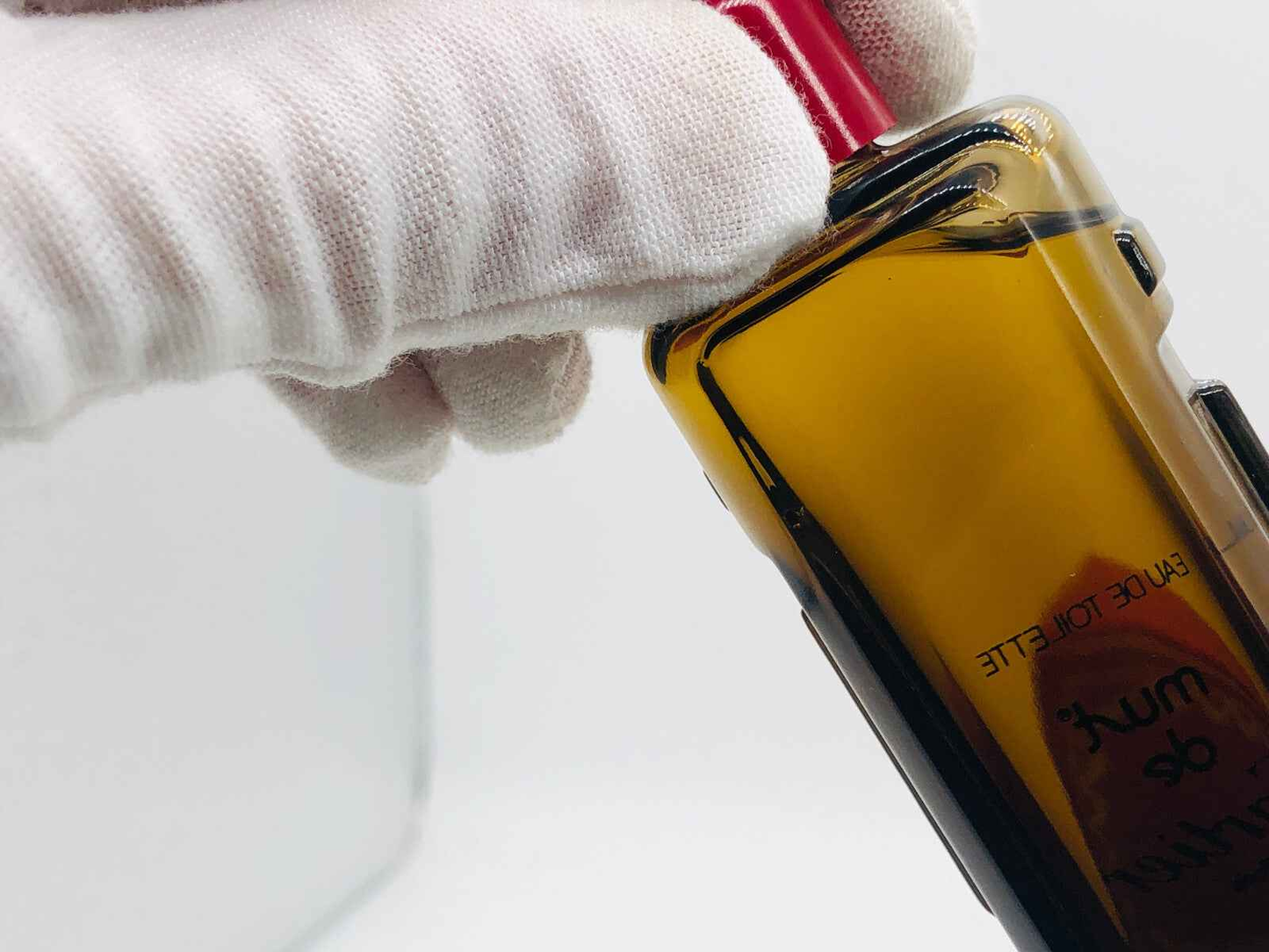 Flacone di profumo Must De Cartier Vintage con tappo rosso, mano in guanto bianco in primo piano