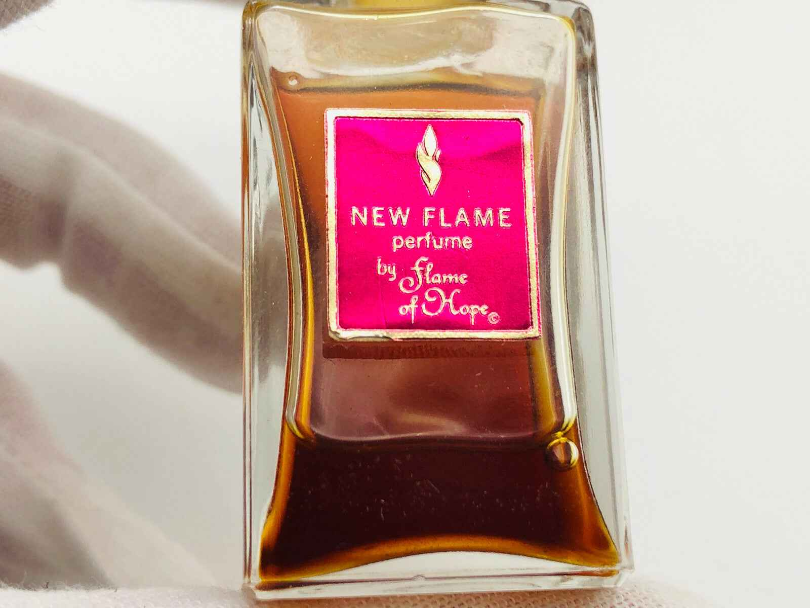 Flame Of Hope Parfum in elegante flacone con etichetta rosa e liquido ambrato
