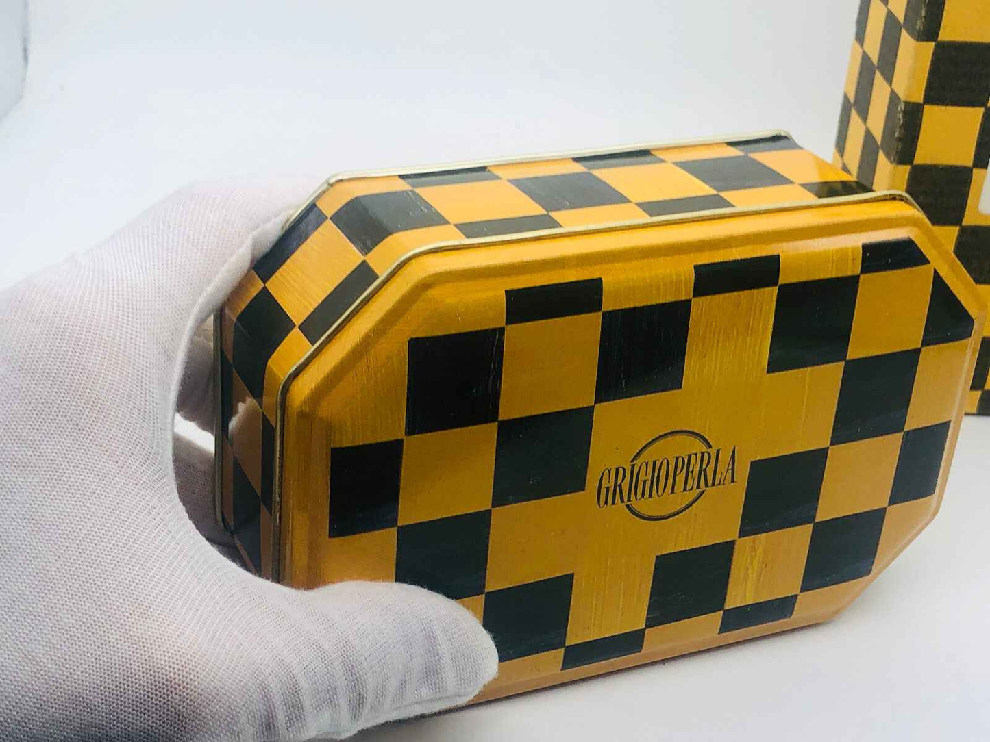 Scatola vintage del profumo Grigioperla con design a scacchi neri e gialli, maneggiata con cura