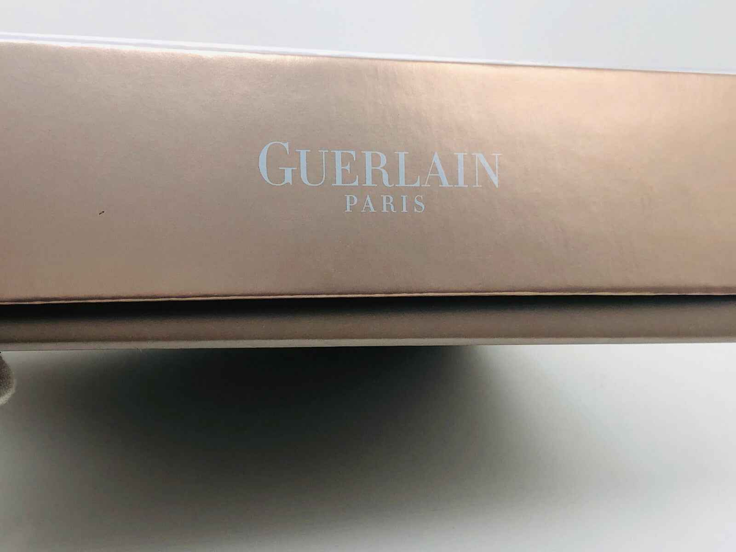 Scatola del profumo Guerlain L'Instant con logo elegante su sfondo beige lucido