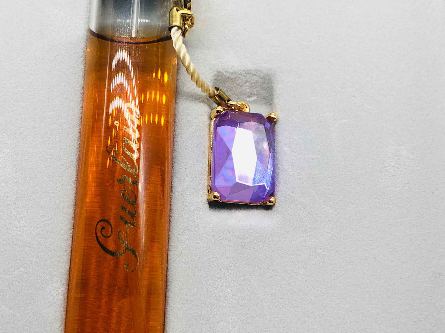 Flacone di profumo Guerlain L'Instant con un ciondolo di gemma viola brillante