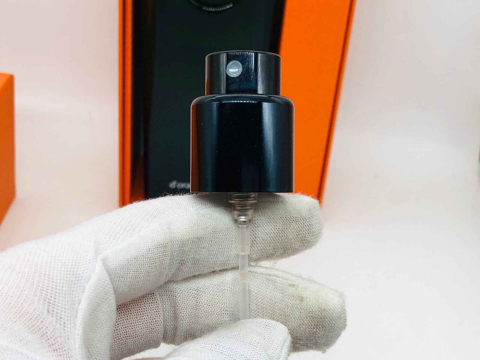 Flacone di Hermes Eau D'Orange Verte con erogatore nero e guanto bianco nella mano