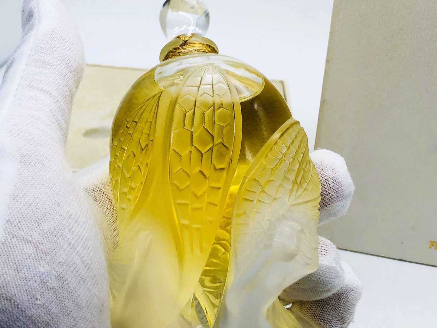 Flacone di profumo Lalique Les Elfes con design elegante e colori caldi, tenuto con cura in una mano guantata