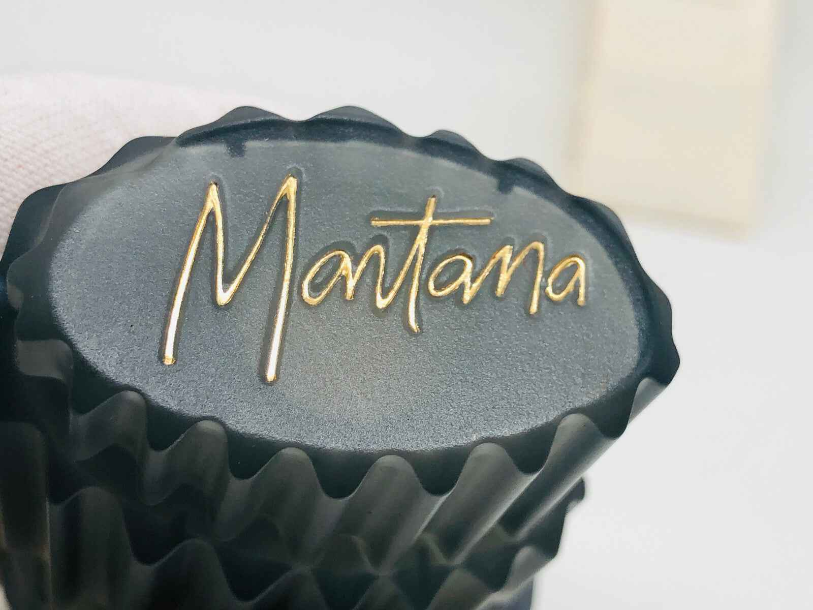 Dettaglio della parte superiore del flacone di profumo vintage MONTANA con logo dorato in rilievo