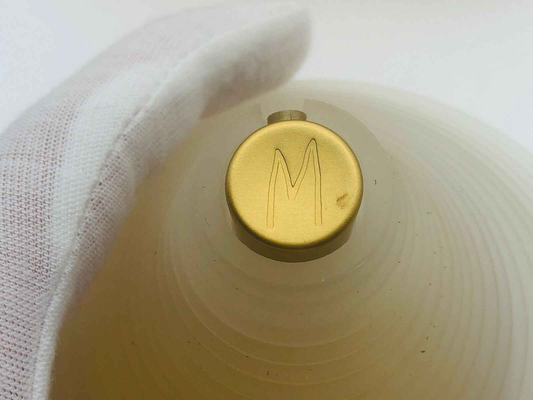 Tappo in oro con lettera M di un profumo Vintage Montana su sfondo chiaro