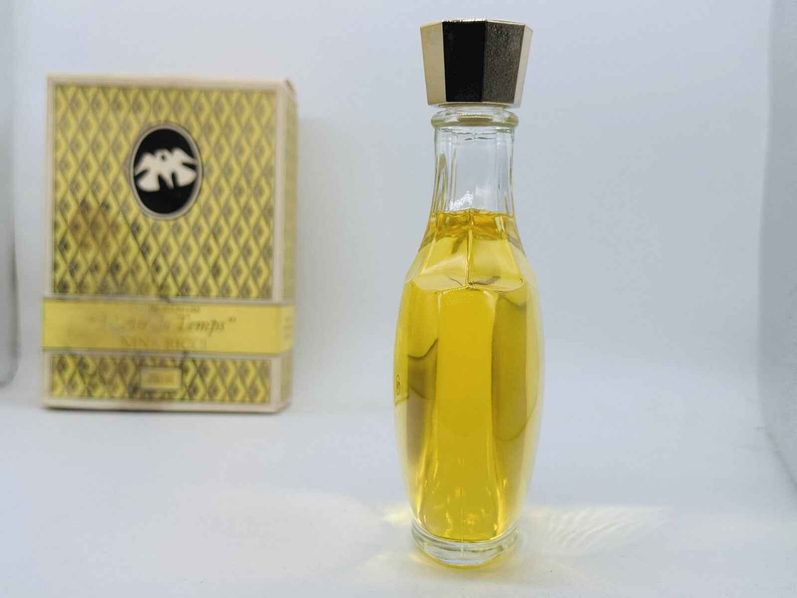 Flacone di Nina Ricci L'Air Du Temps Vintage con tappo dorato e scatola elegante sullo sfondo