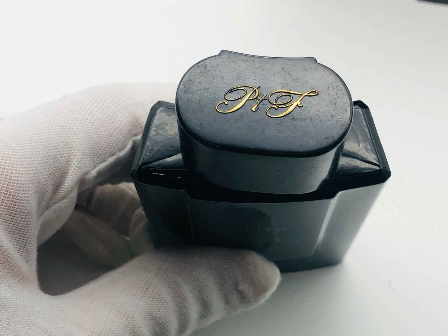 Flacone nero di profumo Arrogance Pour Homme tenuto da mano con guanto bianco su sfondo chiaro