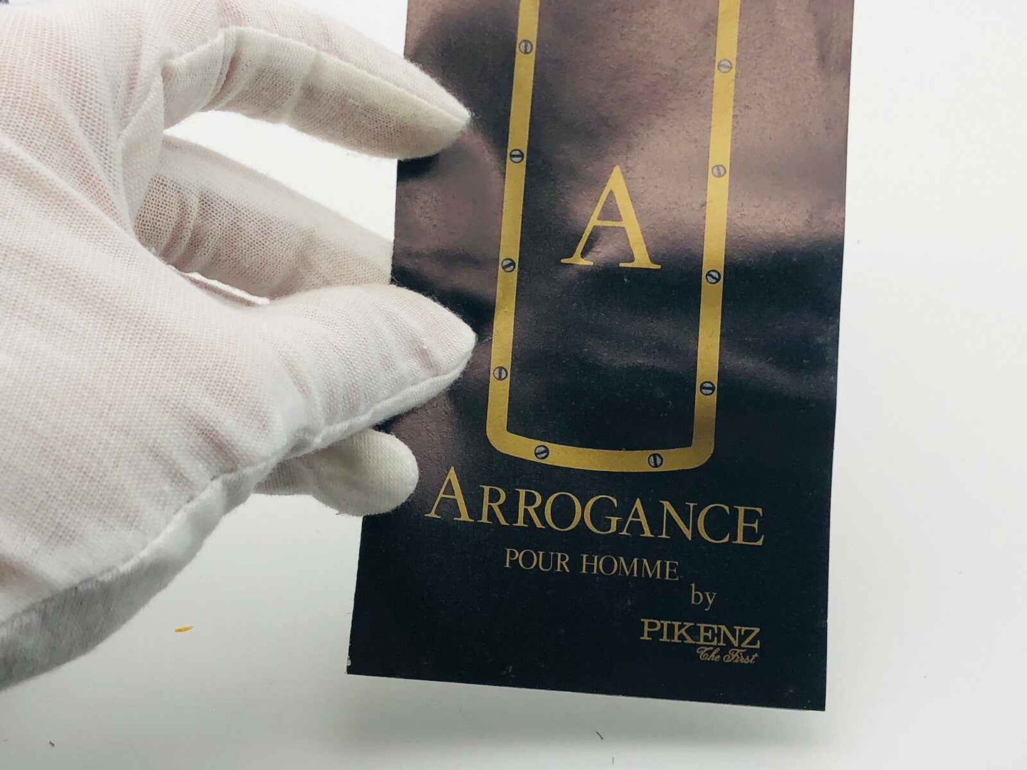 Confezione elegante Arrogance Pour Homme con dettagli dorati tenuta da mano con guanto bianco