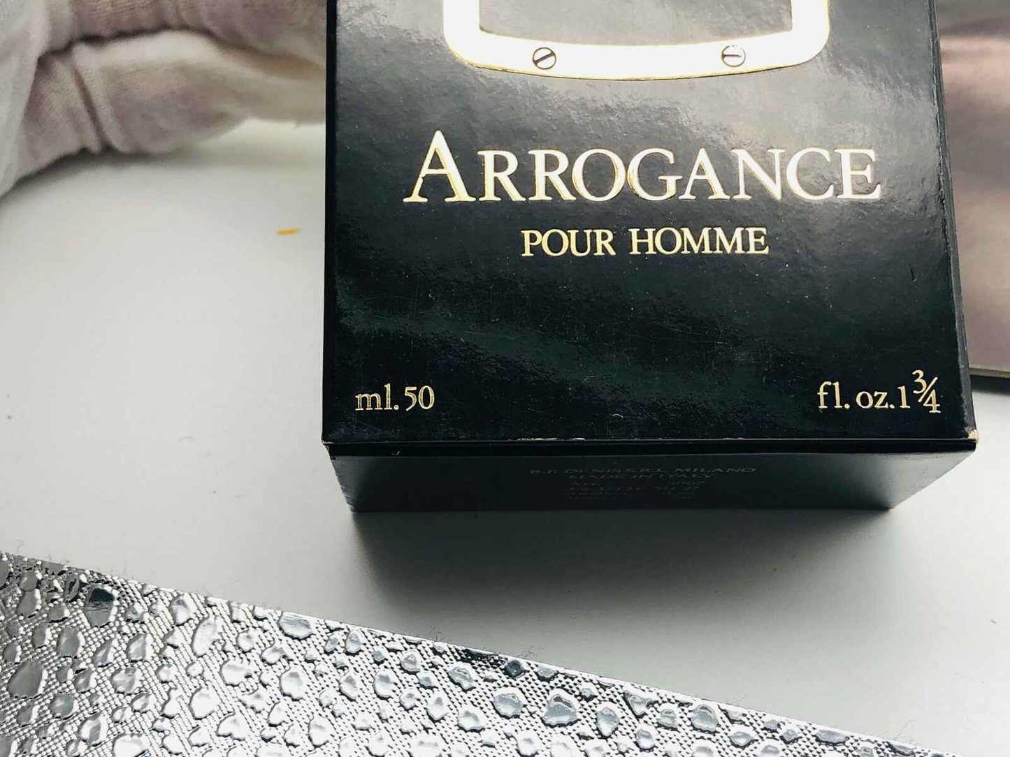 Confezione nera di Arrogance Pour Homme con dettagli dorati da 50 ml sullo sfondo bianco