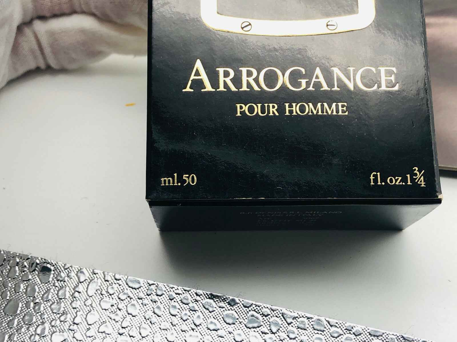Confezione nera di Arrogance Pour Homme con dettagli dorati da 50 ml sullo sfondo bianco