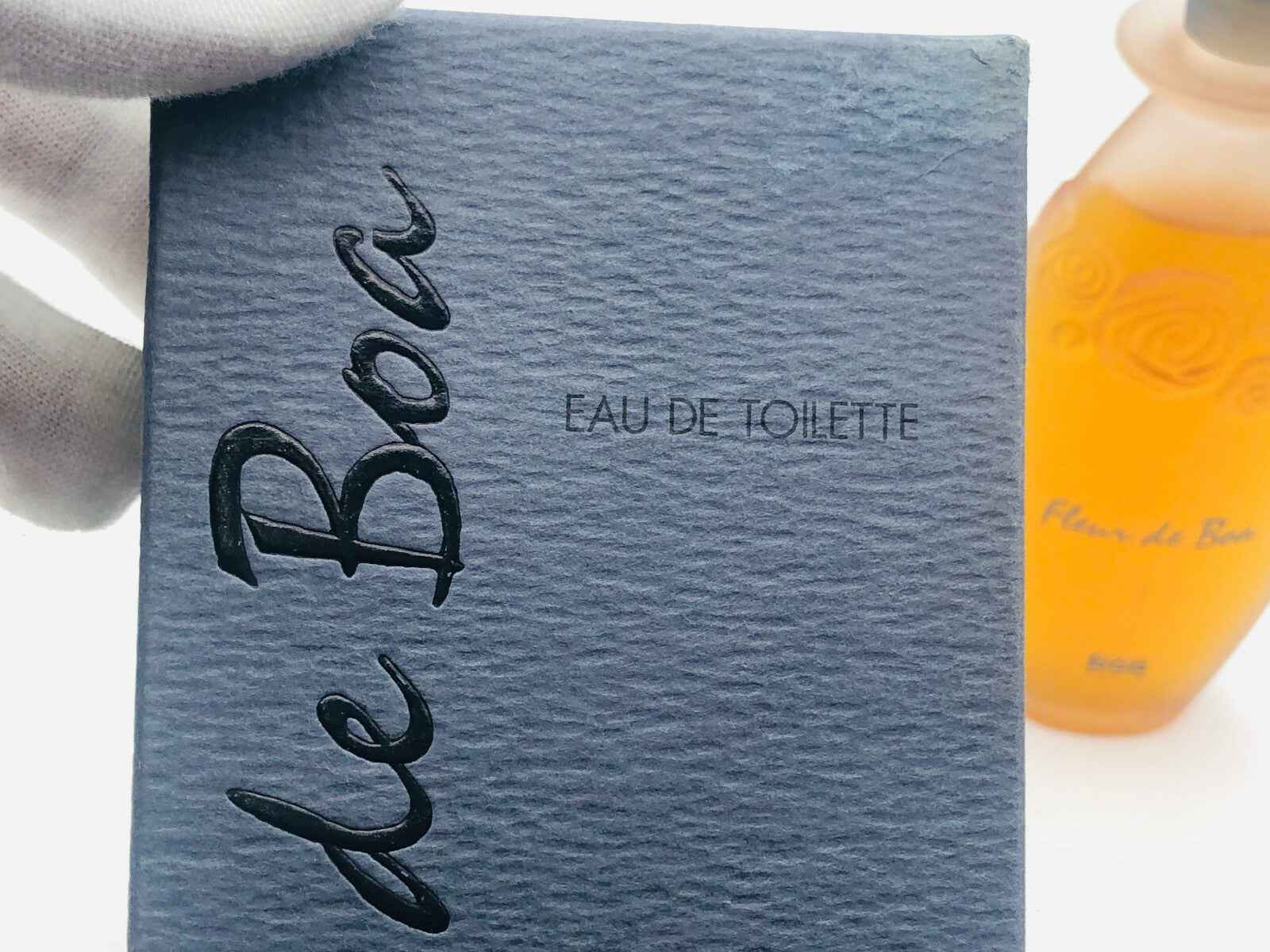 Confezione del Profumo Fleur De Boa con etichetta Eau de Toilette e flacone arancione sullo sfondo