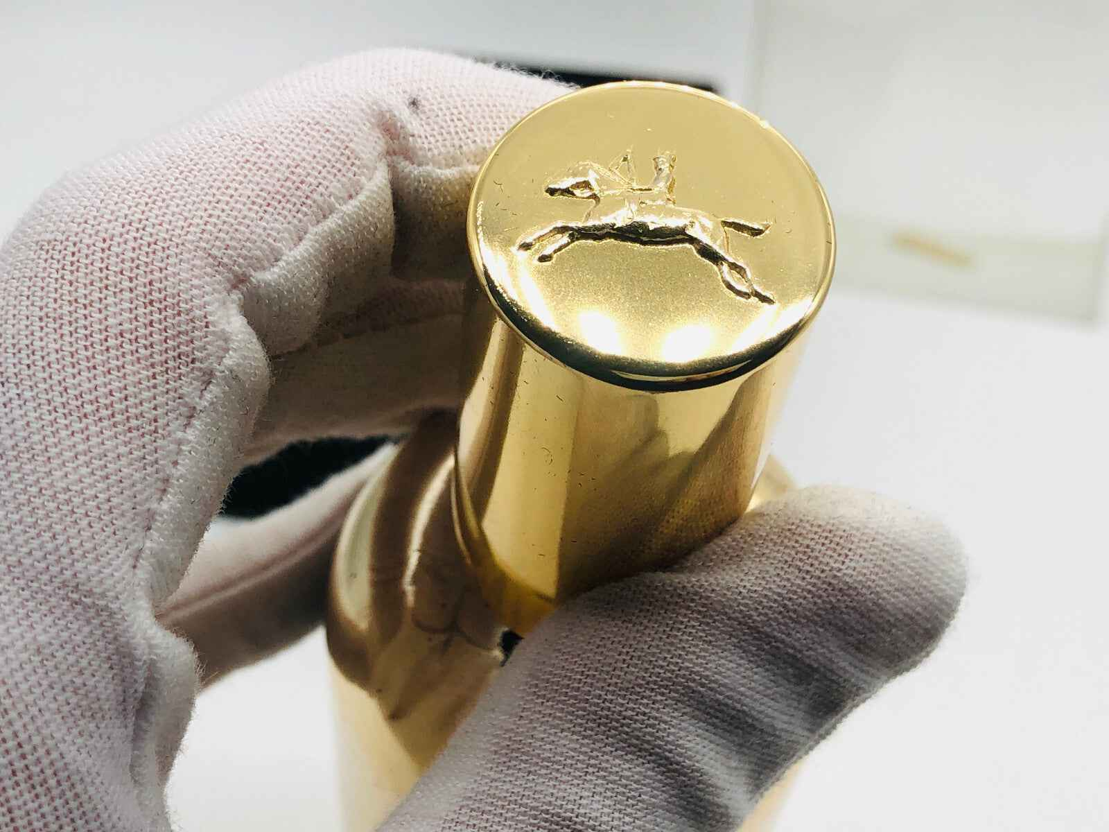 Dettaglio del tappo di profumo Jocelyn Pour Homme in oro con logo in rilievo di un cavallo