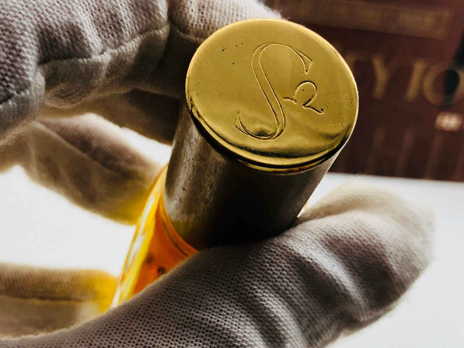 Dettaglio del tappo in oro del profumo Royal Fern, elegante e raffinato, tenuto da una mano bianca.