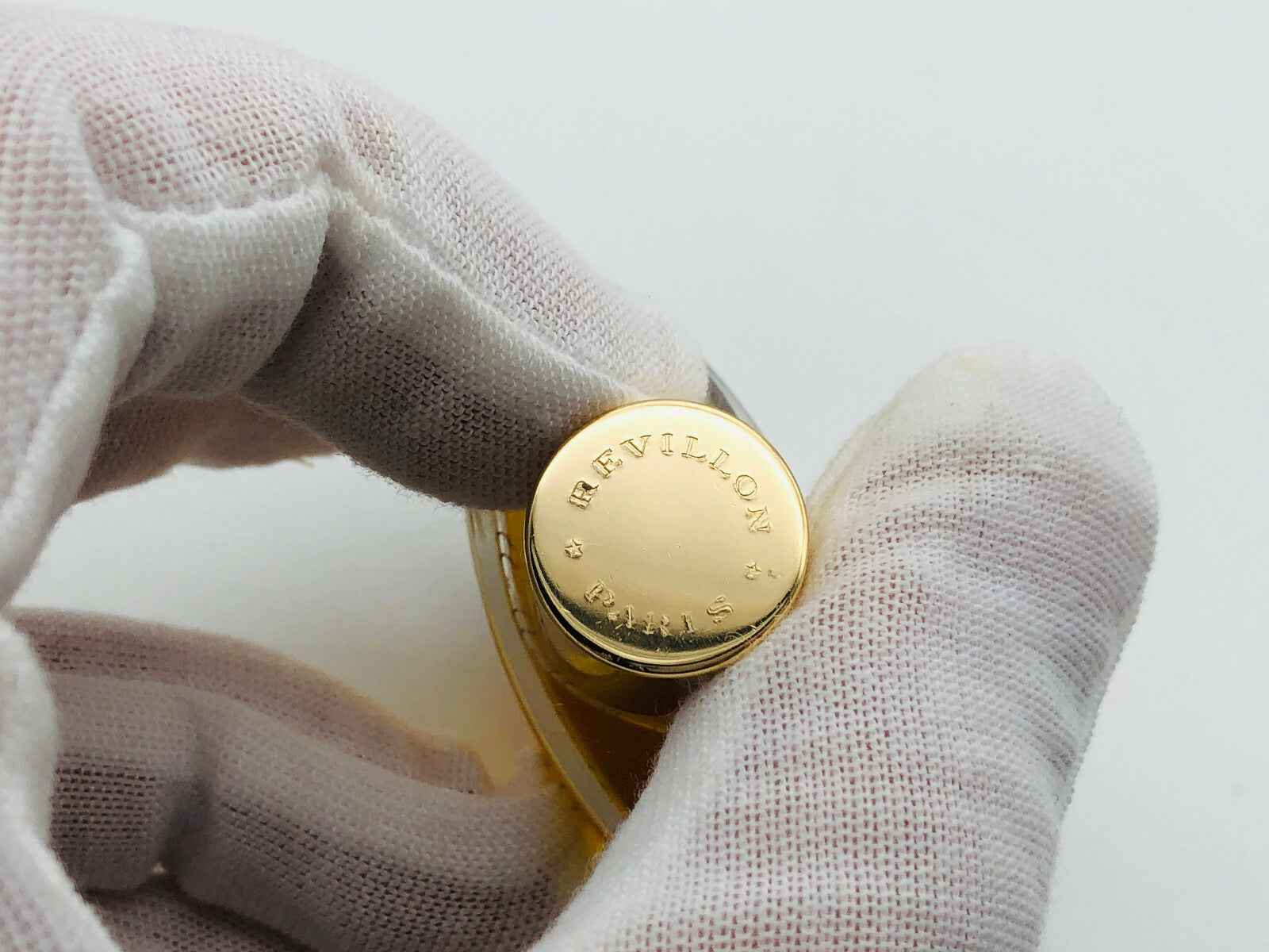 Flacone di profumo Revillon Carnet De Bal con tappo dorato e design elegante in una mano guantata