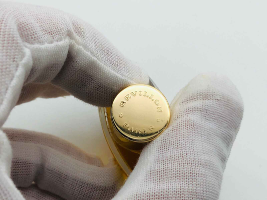 Flacone di profumo Revillon Carnet De Bal con tappo dorato e design elegante in una mano guantata