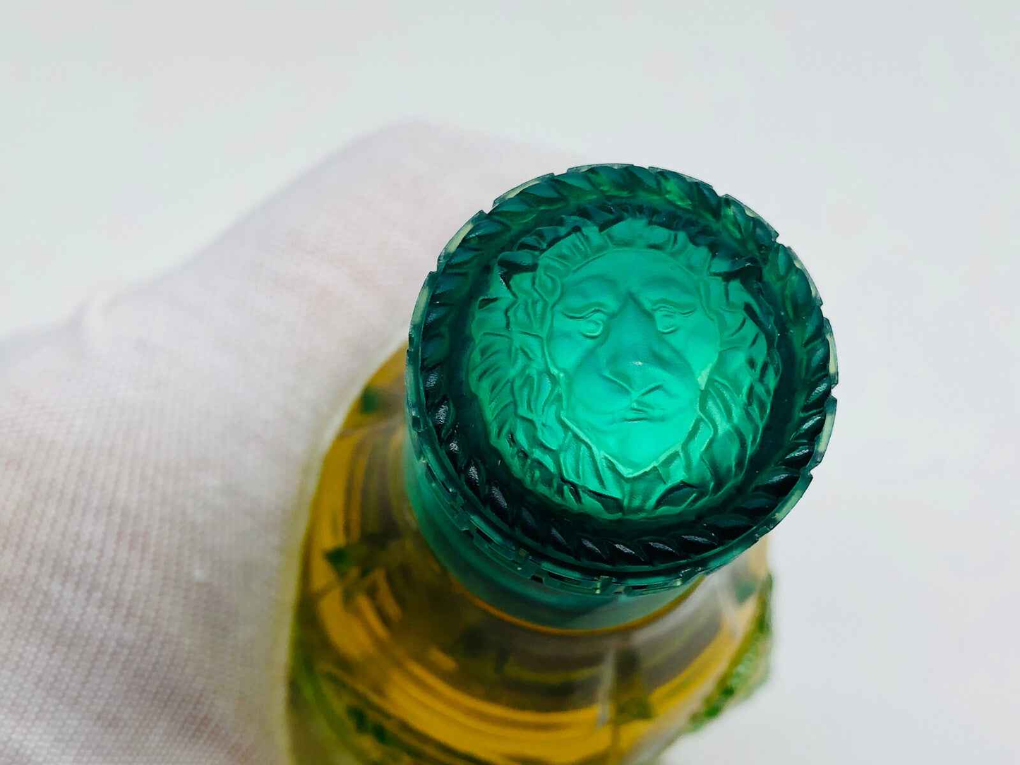 Dettaglio del tappo del profumo Versace Green Jeans con incisione di leone e colore verde brillante