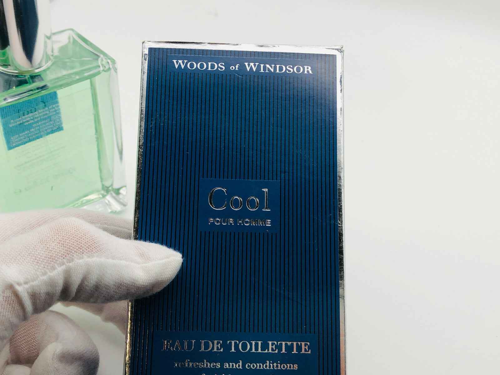 Confezione blu di Woods Of Windsor Cool Eau de Toilette con mano guantata che la tiene