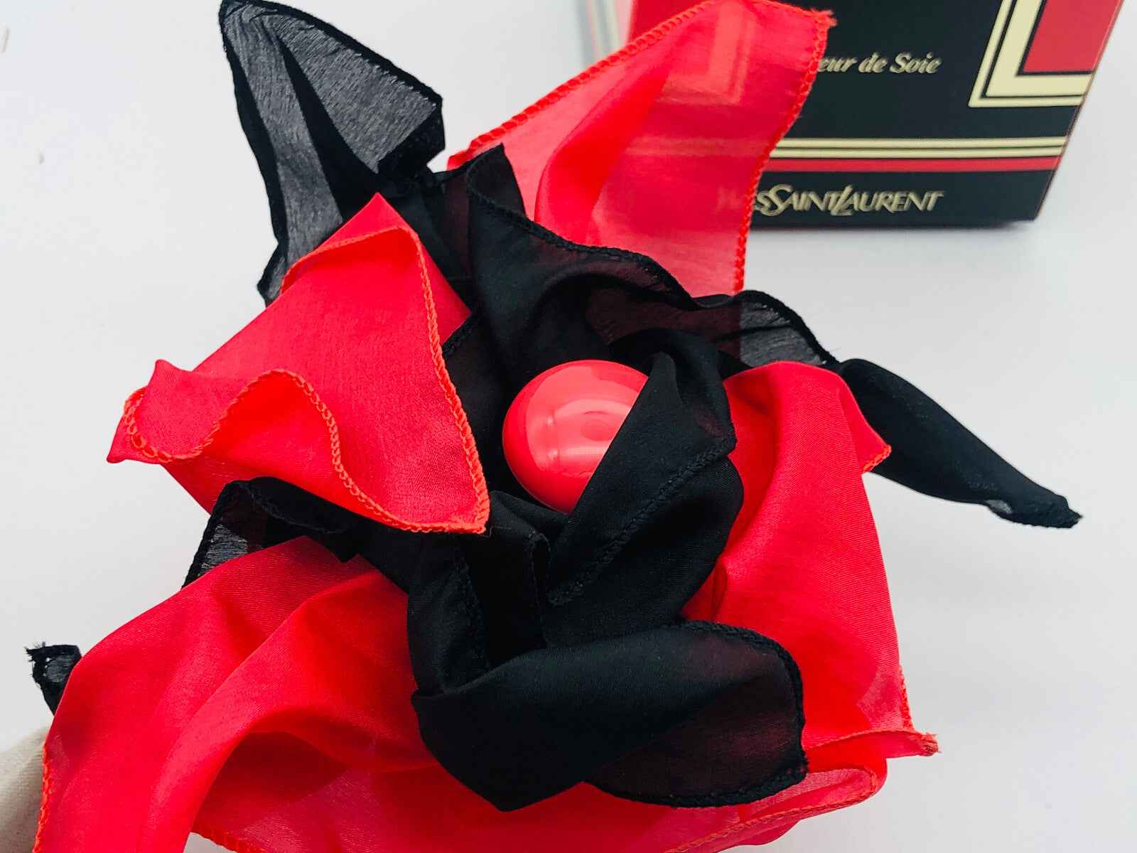 Fiori di seta neri e rossi con flacone di profumo Vintage Ysl Paris al centro per una presentazione elegante