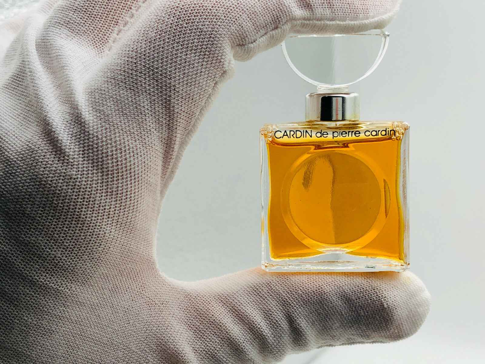 Flacone di profumo CARDIN de pierre cardin vintage con liquidità dorata in una mano guantata