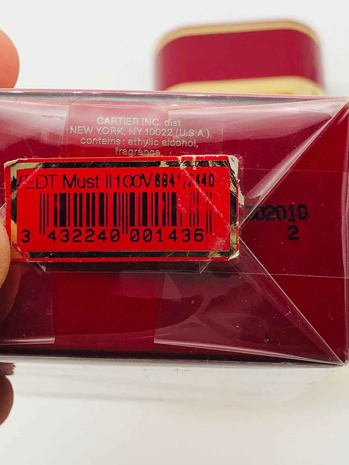 Scatola di Profumo Must De Cartier con etichetta rossa e codice a barre, contenente fragranza raffinata
