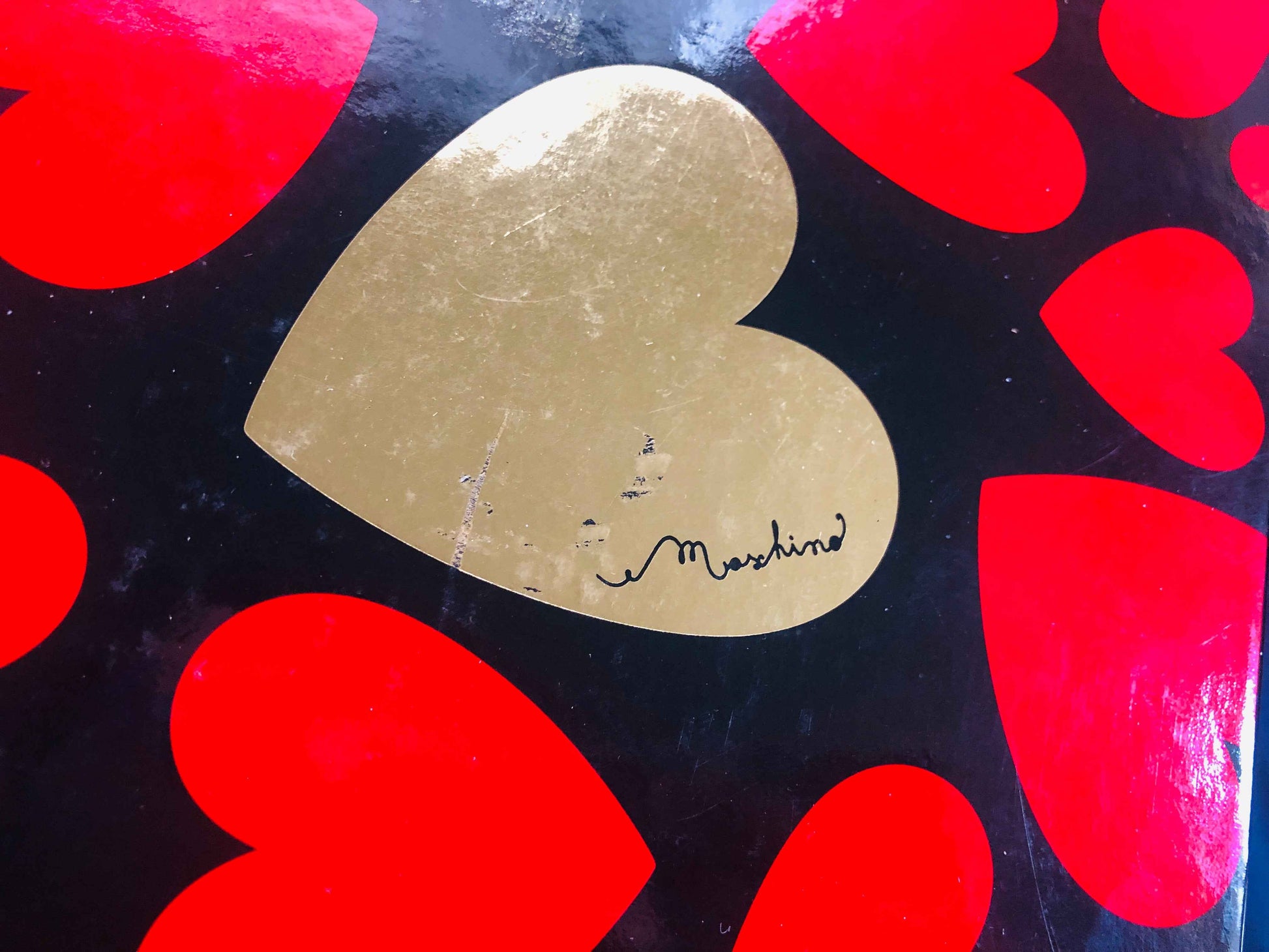 Confezione del profumo Moschino Donna con design a cuori rossi su sfondo nero e cuore dorato