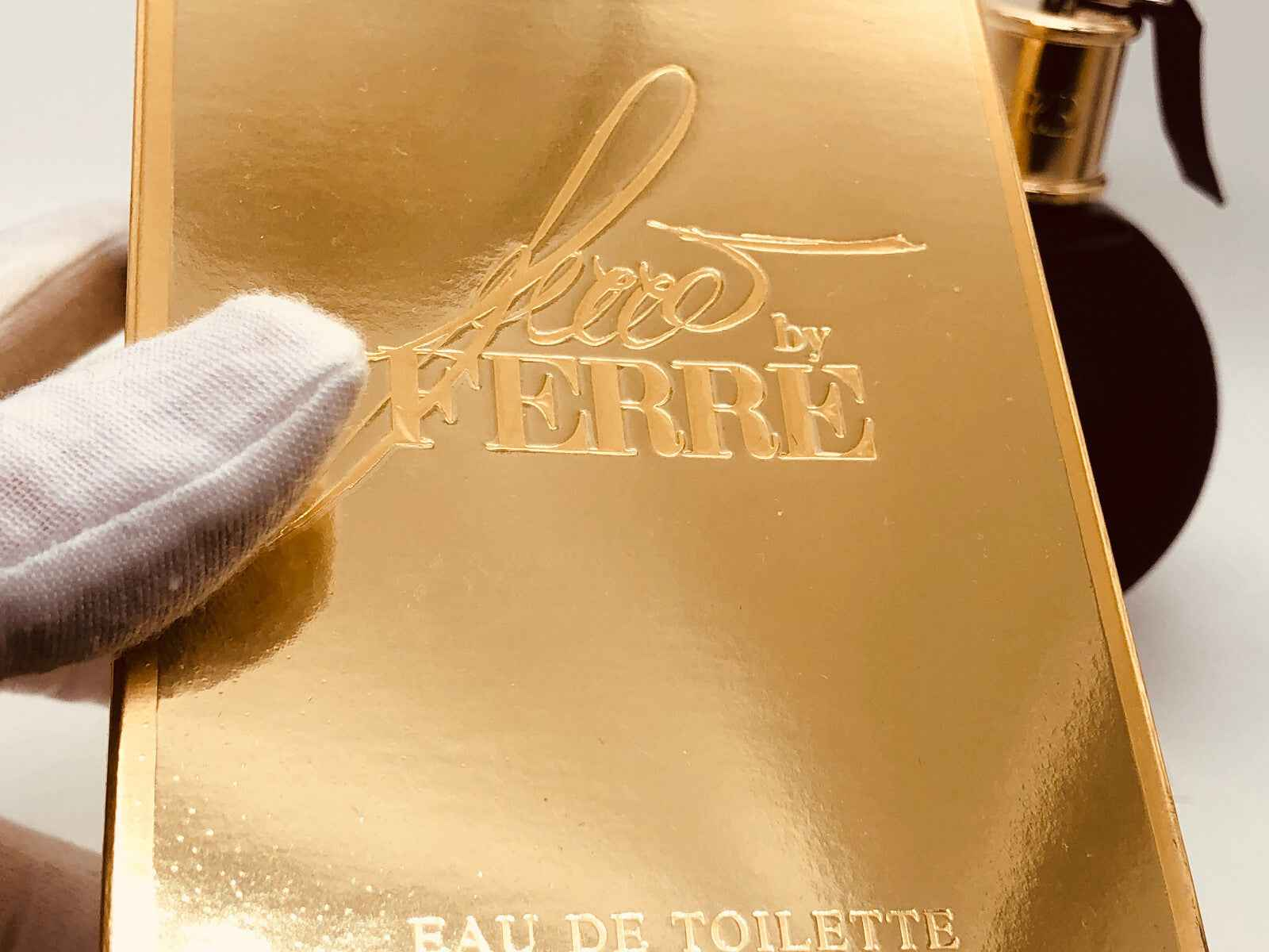 Scatola dorata del profumo Ferre By Ferre Vintage con eleganti dettagli e flacone sullo sfondo