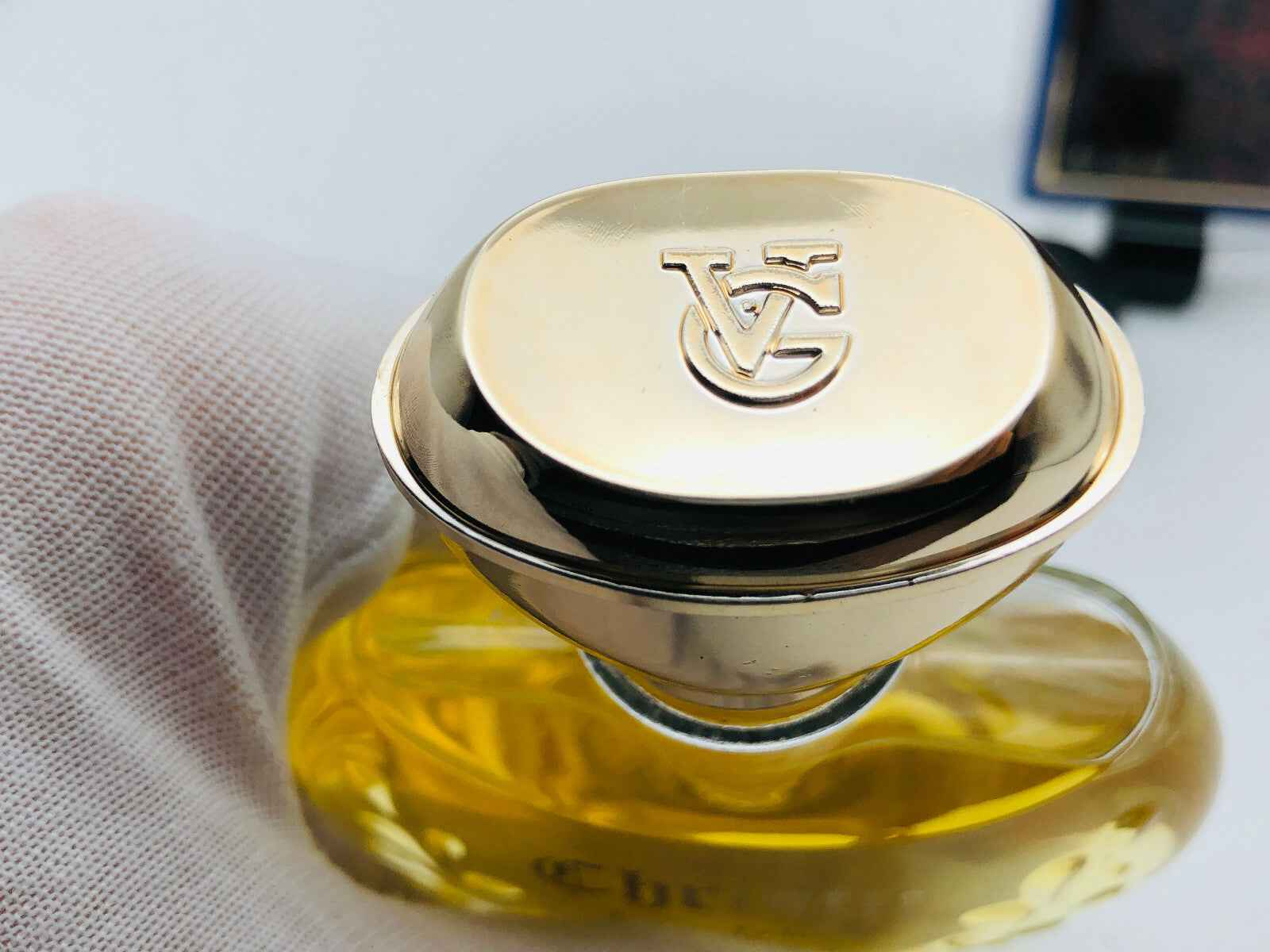 Dettaglio del tappo del profumo Veejaga Christie con logo dorato su fondo giallo